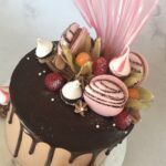 Chocolate drip cake decorated with macarons, meringue kisses, flake, fresh raspberries and rice paper sail