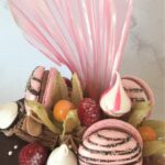 Chocolate drip cake decorated with macarons, meringue kisses, flake, fresh raspberries and rice paper sail