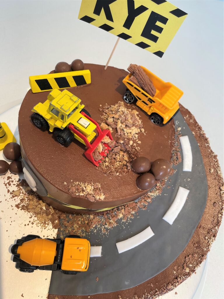 Digger Cake decorated with crushed biscuits and chocolate for a sand/mud effect and chocolate boulders