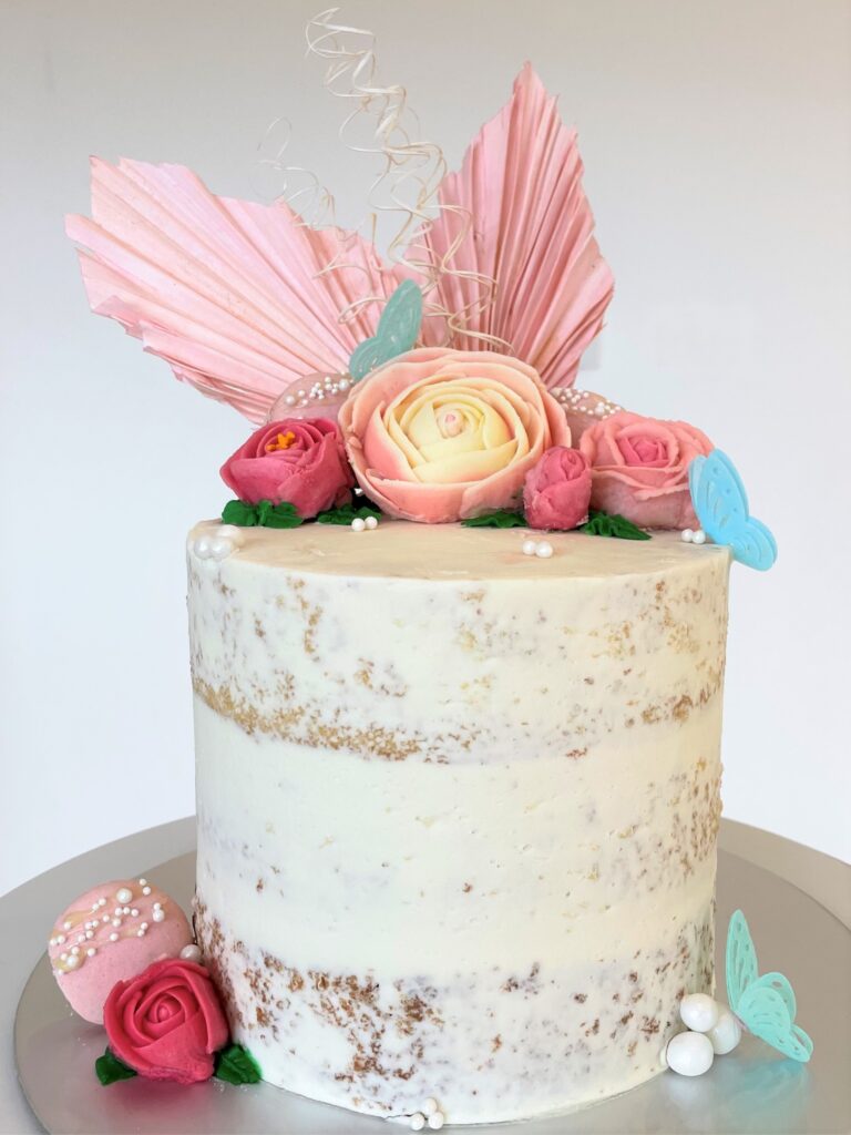 Naked cake decorated with buttercream flowers and macarons, finished with pearls and rice paper butterflies