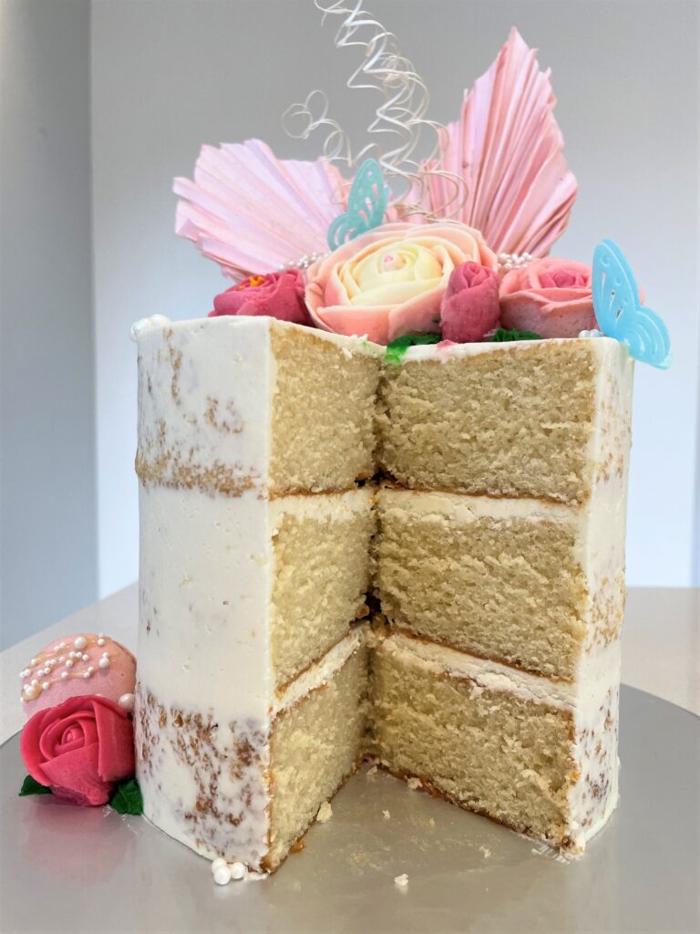 Naked cake decorated with buttercream flowers and macarons, finished with pearls and rice paper butterflies