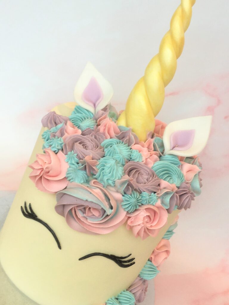 Decorated with swirls of colourful buttercream , fondant ears, lashes and golden horn