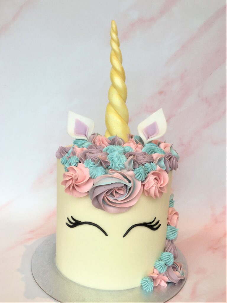 Unicorn cake with swirls of colourful buttercream and edible fondant ears and horn