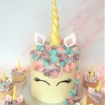 Unicorn cake with swirls of colourful buttercream and edible fondant ears and horn and matching cupcakes