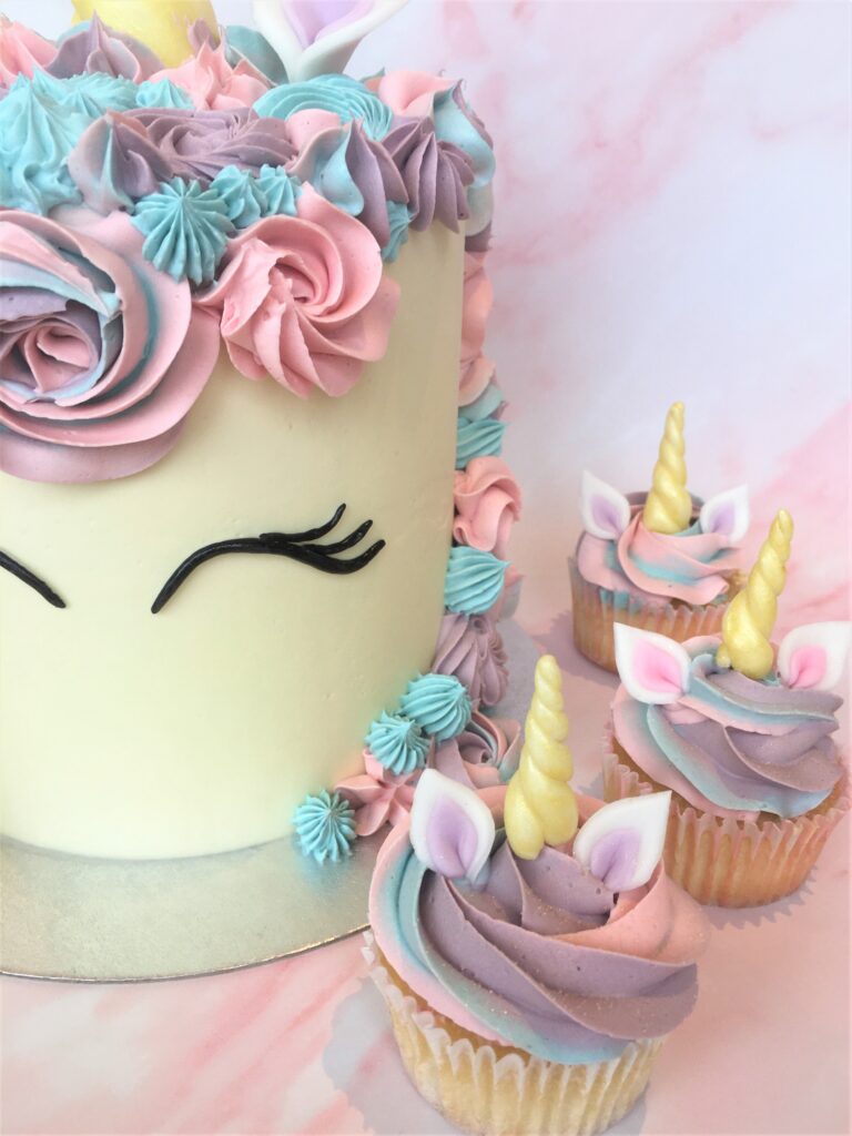 Unicorn cake with swirls of colourful buttercream and edible fondant ears and horn and matching cupcakes