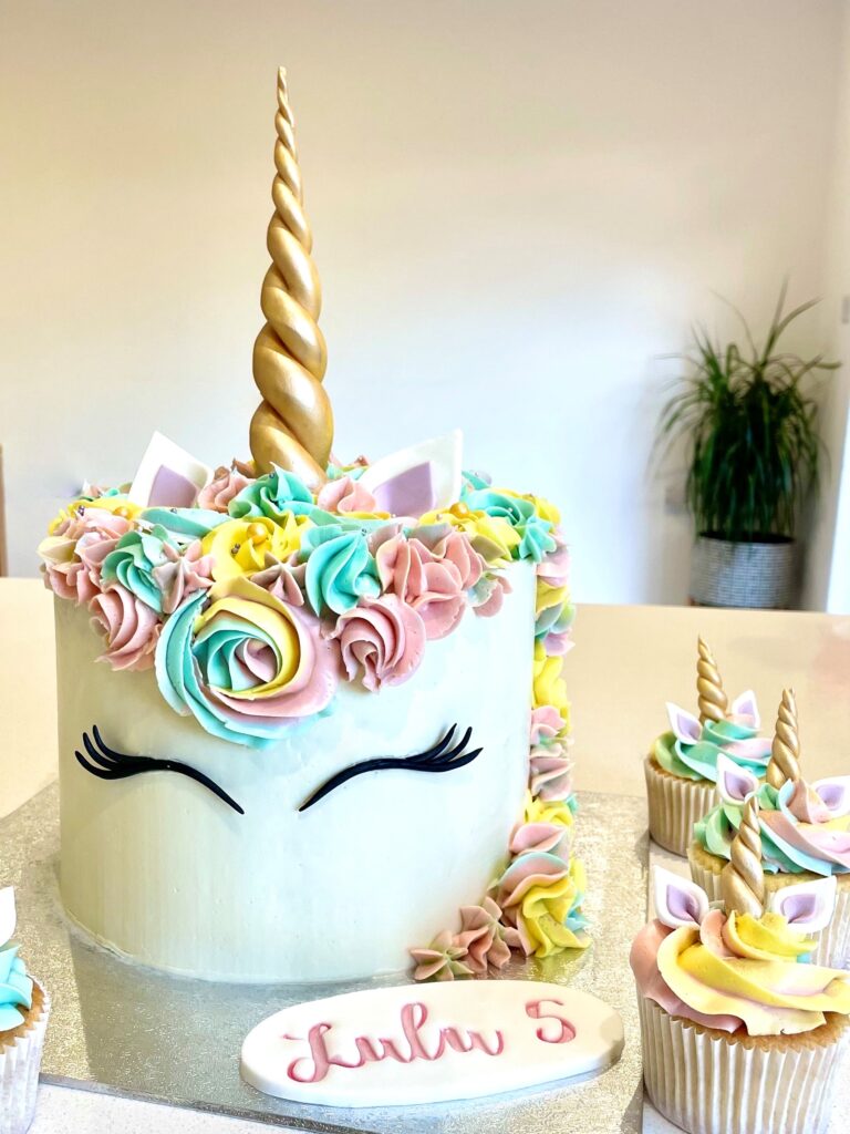 Decorated with swirls of colourful buttercream , fondant ears, lashes and golden horn