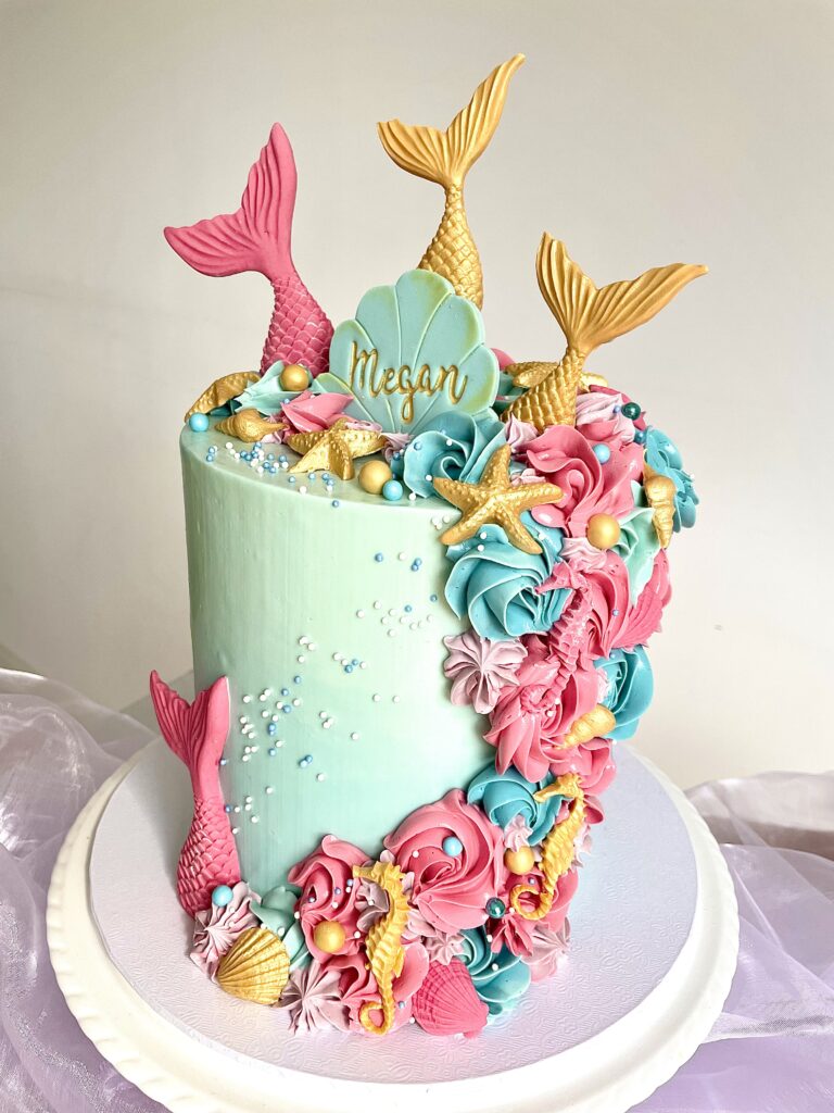 Decorated with colourful buttercream swirls, fondant tails and shells, with personalised oyster shell name sign